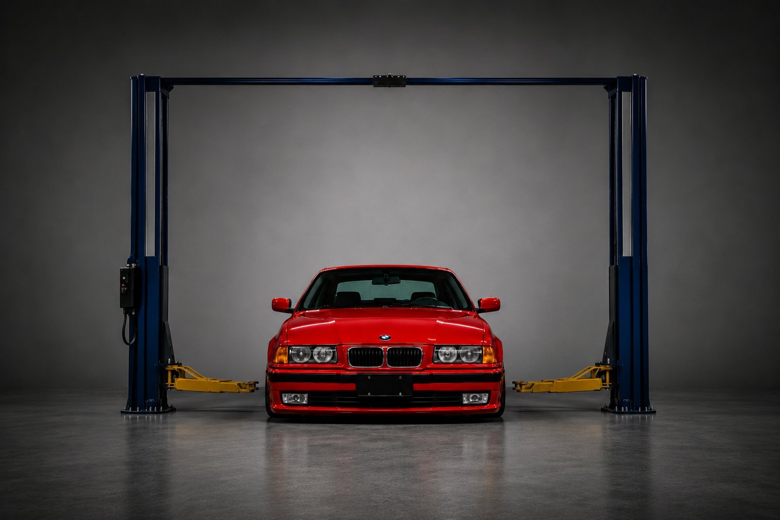 Red sports car lifted on a two-post hydraulic lift in an automotive repair garage with gray walls