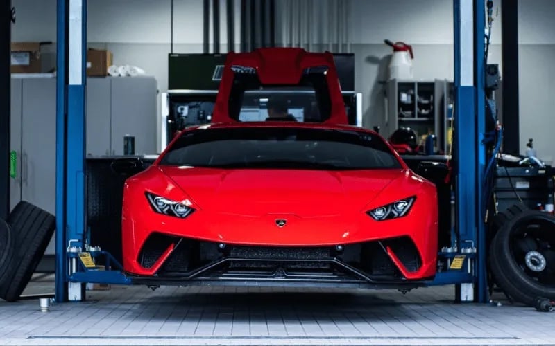 Bright red high-performance sports car lifted on a hydraulic lift in a modern automotive service garage