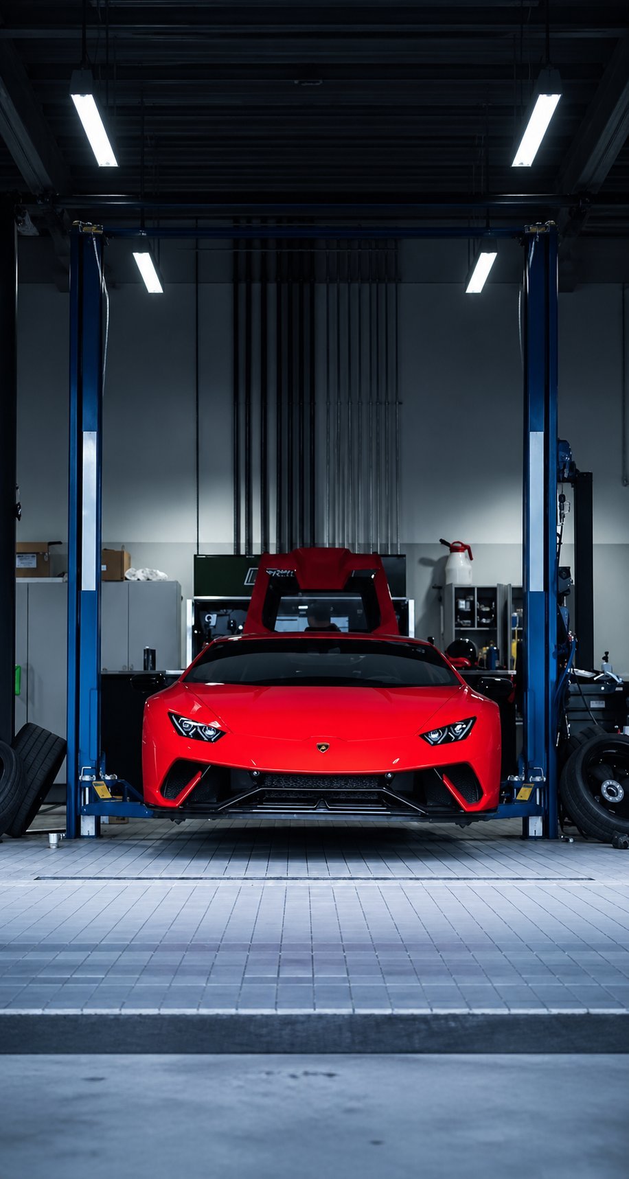 Red sports car lifted on hydraulic lift in modern automotive service garage with blue pillars and LED lighting